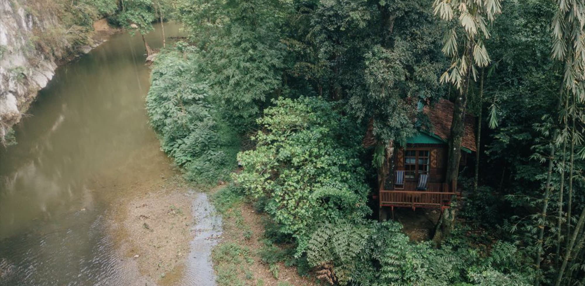 Drone view of treehouse by the river surrounded by jungle